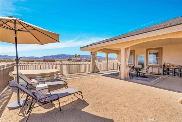 view of patio with outdoor dining space, a covered hot tub, a mountain view, and fence