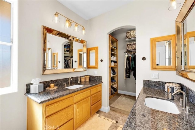 bathroom with a spacious closet, two vanities, a sink, and baseboards