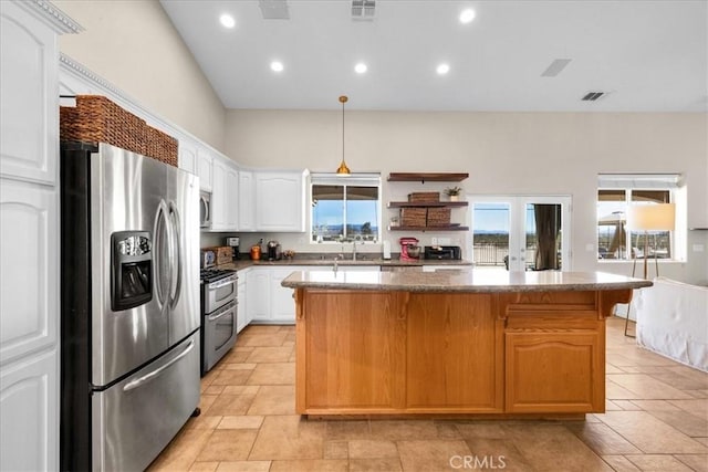 kitchen featuring visible vents, appliances with stainless steel finishes, white cabinets, a kitchen island, and dark stone countertops