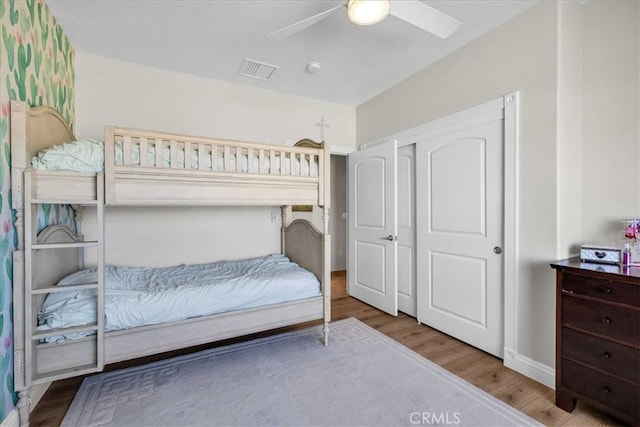 bedroom with baseboards, visible vents, a ceiling fan, wood finished floors, and a closet