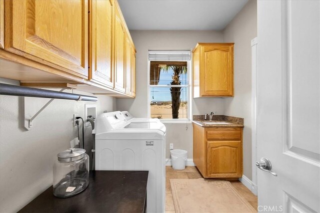 laundry area with cabinet space, light tile patterned floors, baseboards, washer and clothes dryer, and a sink