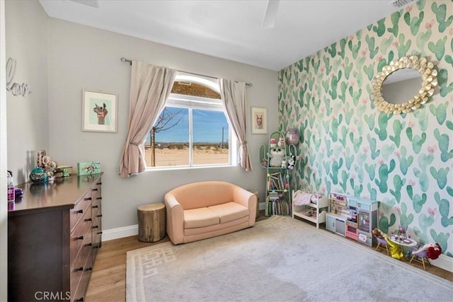 living area with an accent wall, wood finished floors, wallpapered walls, and baseboards