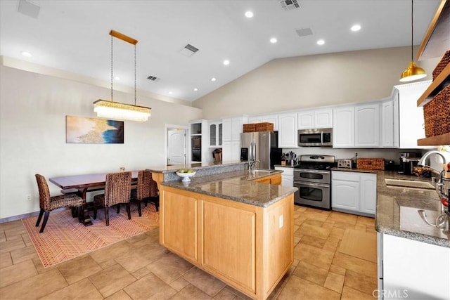 kitchen with a center island with sink, dark stone counters, stainless steel appliances, high vaulted ceiling, and a sink