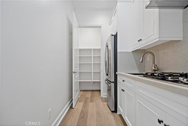 kitchen with light wood-type flooring, freestanding refrigerator, white cabinetry, and wall chimney exhaust hood