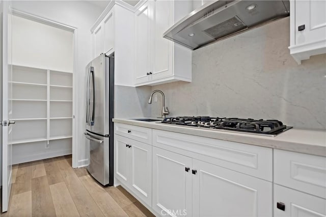 kitchen with white cabinets, wall chimney exhaust hood, appliances with stainless steel finishes, light wood-type flooring, and a sink