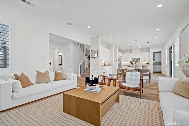 living room featuring light wood-type flooring, ornamental molding, visible vents, recessed lighting, and stairs