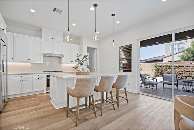 kitchen featuring light wood-style flooring, under cabinet range hood, visible vents, light countertops, and a center island