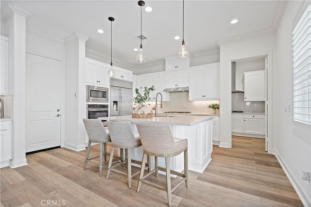 kitchen with ornamental molding, a breakfast bar, built in appliances, under cabinet range hood, and white cabinetry