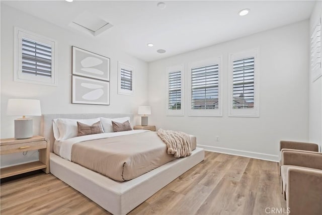 bedroom with baseboards, light wood finished floors, attic access, and recessed lighting