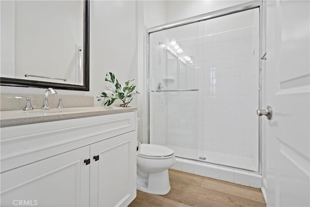 bathroom with toilet, a stall shower, wood finished floors, and vanity