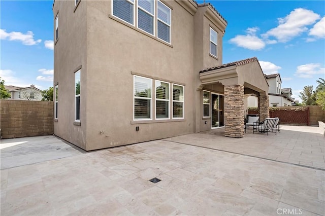 rear view of property featuring a tiled roof, fence, a patio, and stucco siding