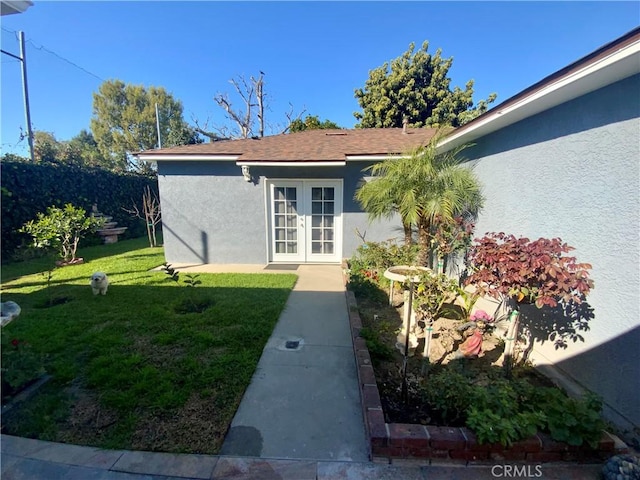 doorway to property with a yard, french doors, roof with shingles, and stucco siding