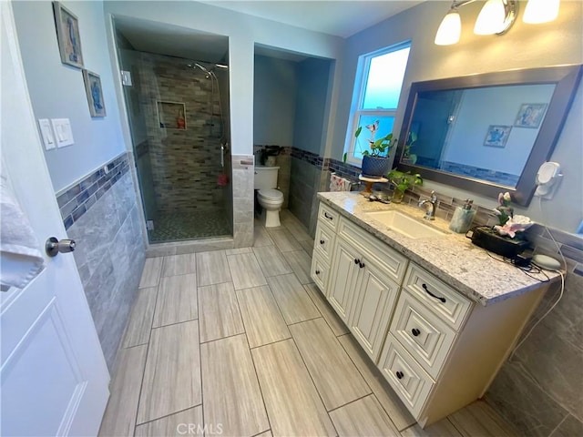 bathroom with a wainscoted wall, toilet, a stall shower, tile walls, and vanity