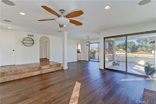 unfurnished living room with visible vents, arched walkways, baseboards, dark wood-style floors, and recessed lighting