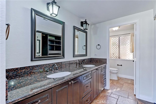 full bathroom featuring double vanity, a sink, toilet, and stone tile floors