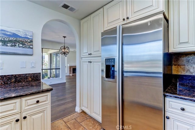 kitchen with stone tile floors, visible vents, white cabinets, arched walkways, and stainless steel refrigerator with ice dispenser