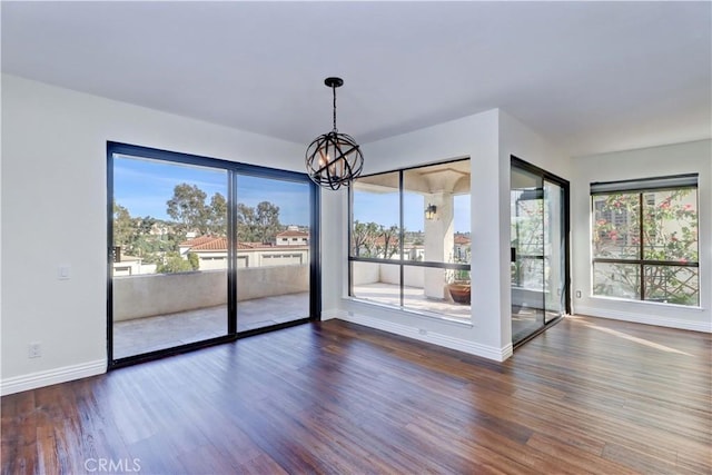 unfurnished dining area with a chandelier, wood finished floors, a wealth of natural light, and baseboards