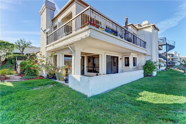 back of house featuring a lawn, a balcony, and stucco siding