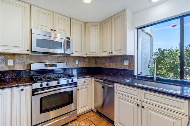 kitchen with dark stone counters, stainless steel appliances, backsplash, and a sink