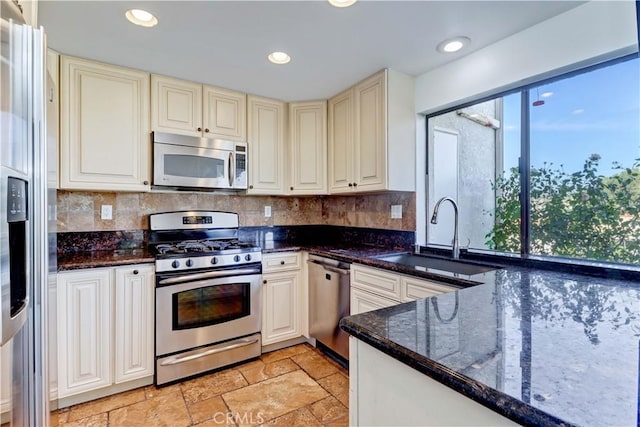 kitchen featuring stainless steel appliances, a sink, dark stone counters, tasteful backsplash, and stone tile flooring