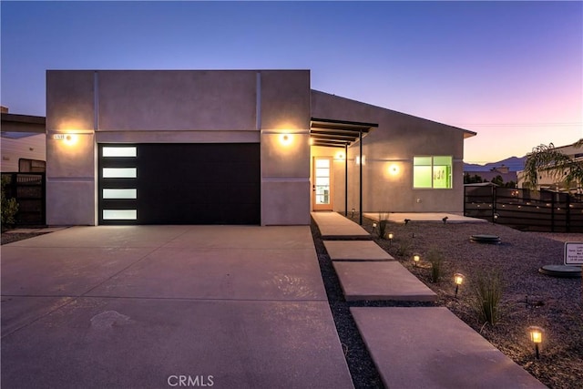 modern home with stucco siding, driveway, an attached garage, and fence