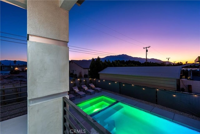 pool at dusk featuring a pool with connected hot tub and a fenced backyard