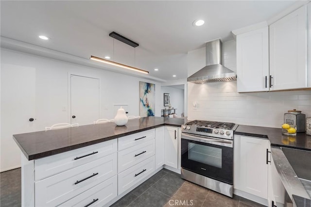 kitchen featuring wall chimney range hood, stainless steel gas range oven, white cabinetry, and decorative backsplash