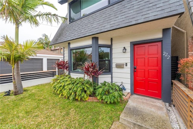 entrance to property featuring a garage, roof with shingles, and a lawn