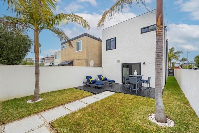 rear view of property with a yard, a fenced backyard, a deck, and stucco siding