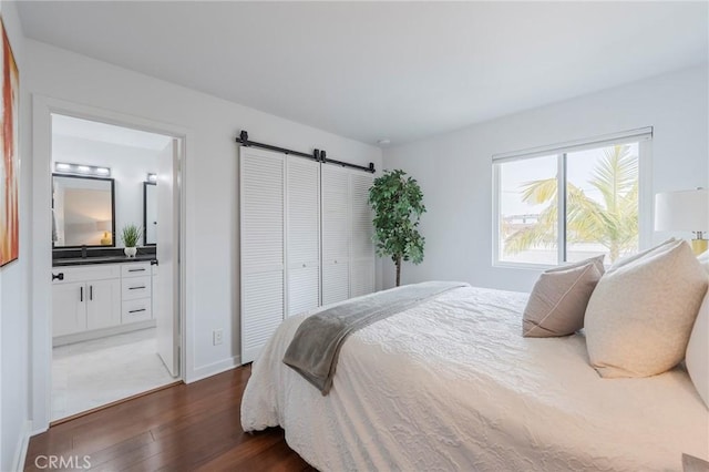 bedroom with a barn door, baseboards, wood finished floors, ensuite bathroom, and a sink