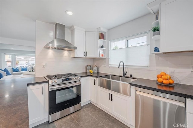 kitchen featuring dark countertops, wall chimney exhaust hood, appliances with stainless steel finishes, open shelves, and a sink