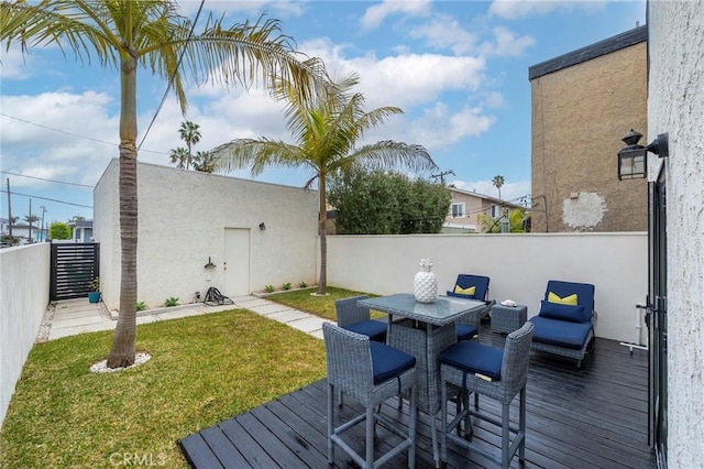 wooden terrace featuring outdoor dining space, a fenced backyard, and a lawn