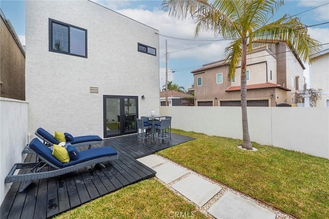 back of property with fence private yard, a wooden deck, a lawn, and stucco siding