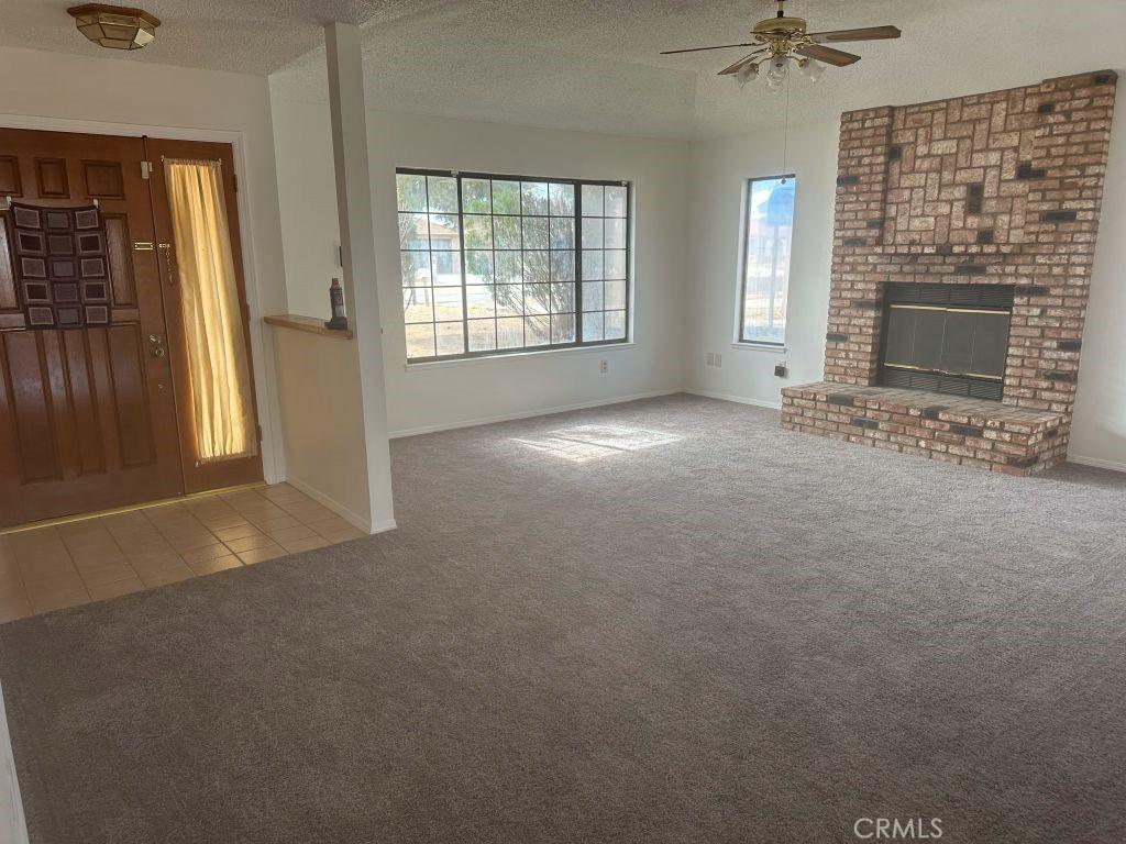 unfurnished living room with a textured ceiling, a fireplace, baseboards, tile patterned floors, and carpet