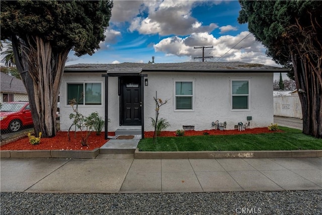 bungalow-style house with stucco siding, roof with shingles, crawl space, fence, and a front yard