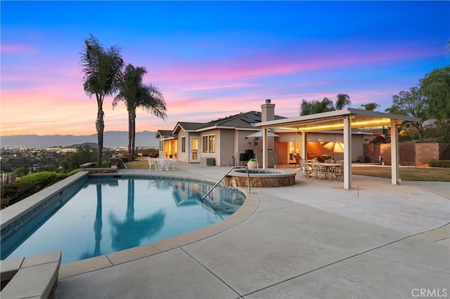 pool at dusk with outdoor dining space, an outdoor pool, a patio, and an in ground hot tub