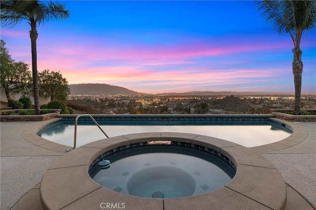 pool at dusk with an in ground hot tub, a mountain view, and an outdoor pool