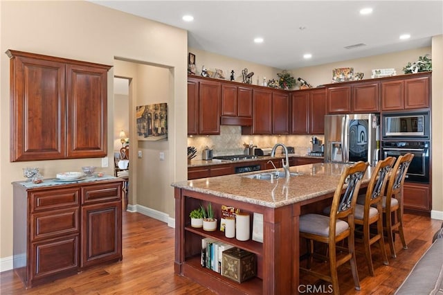 kitchen with appliances with stainless steel finishes, wood finished floors, a sink, under cabinet range hood, and backsplash