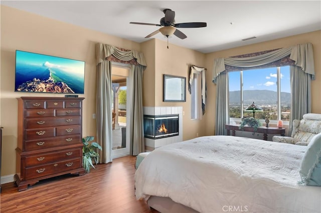 bedroom with visible vents, a glass covered fireplace, wood finished floors, access to exterior, and a mountain view