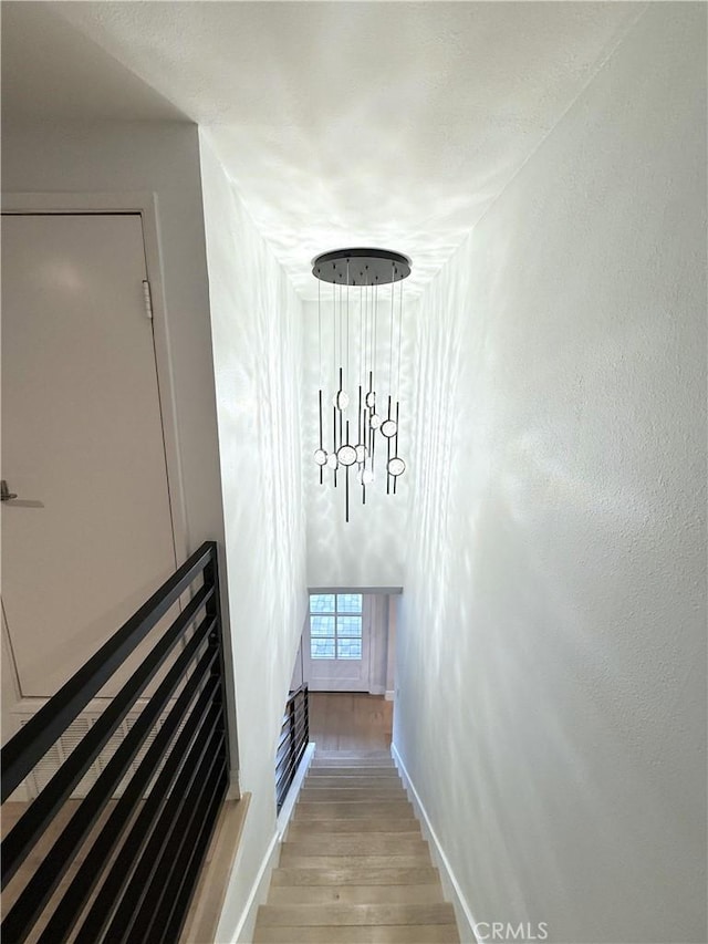 stairway featuring a chandelier, baseboards, and wood finished floors