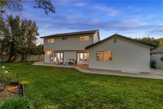 back of property at dusk featuring french doors, a fenced backyard, a patio, and stucco siding