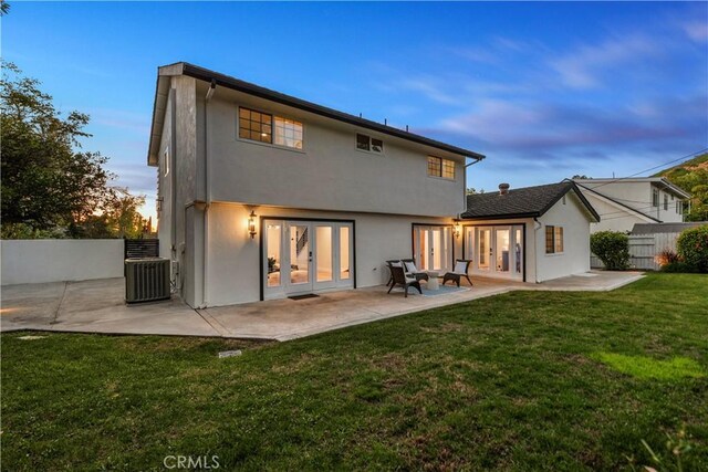 back of property at dusk with a yard, stucco siding, a patio, fence, and french doors