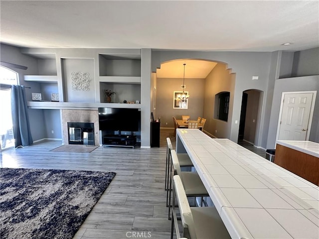 living area with built in shelves, a glass covered fireplace, wood finished floors, a chandelier, and baseboards