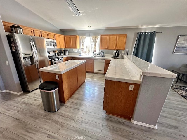 kitchen with tile countertops, appliances with stainless steel finishes, a center island, a peninsula, and vaulted ceiling