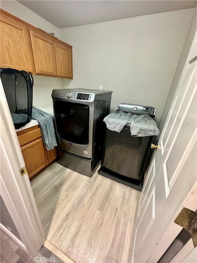 washroom with independent washer and dryer, light wood-type flooring, and cabinet space