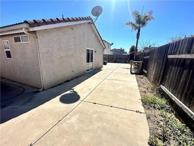 view of side of home featuring a patio, a fenced backyard, and stucco siding