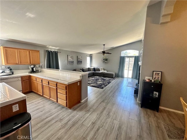 kitchen with tile counters, lofted ceiling, light wood-type flooring, dishwasher, and a peninsula