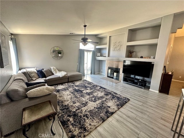 living room featuring a fireplace, wood finished floors, a ceiling fan, baseboards, and built in features