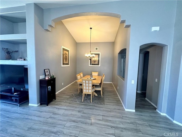 dining space featuring arched walkways, built in shelves, wood finished floors, and lofted ceiling