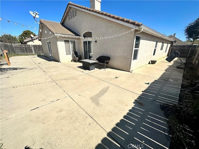 back of house featuring a fenced backyard, a patio, a tiled roof, and stucco siding